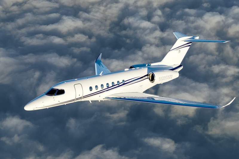 Aeronave Cessna Citation Longitude, na cor branca, voando sobre as nuvens em um dia ensolarado.